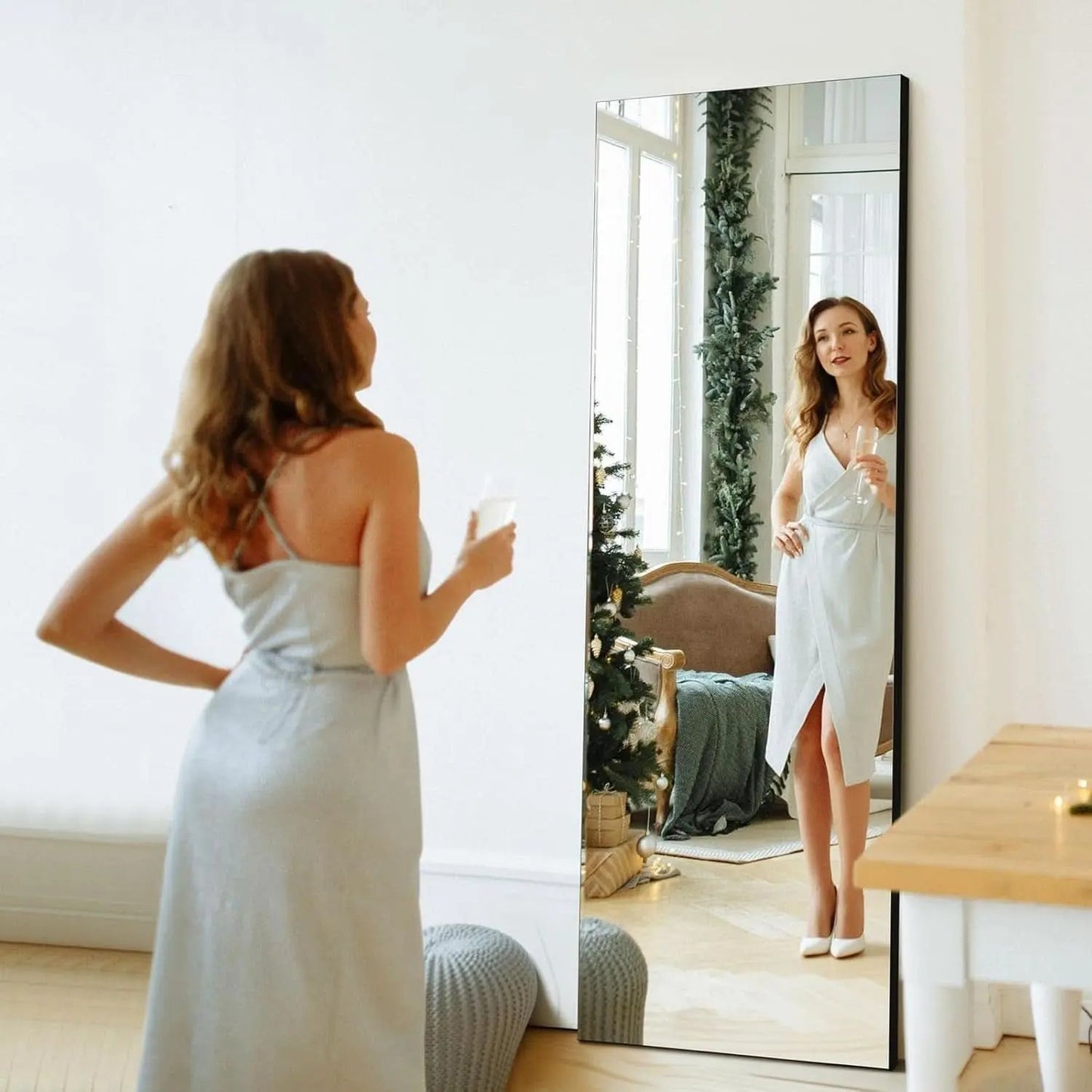 Woman in a white dress standing in front of a full-length mirror in a room with a Christmas tree.