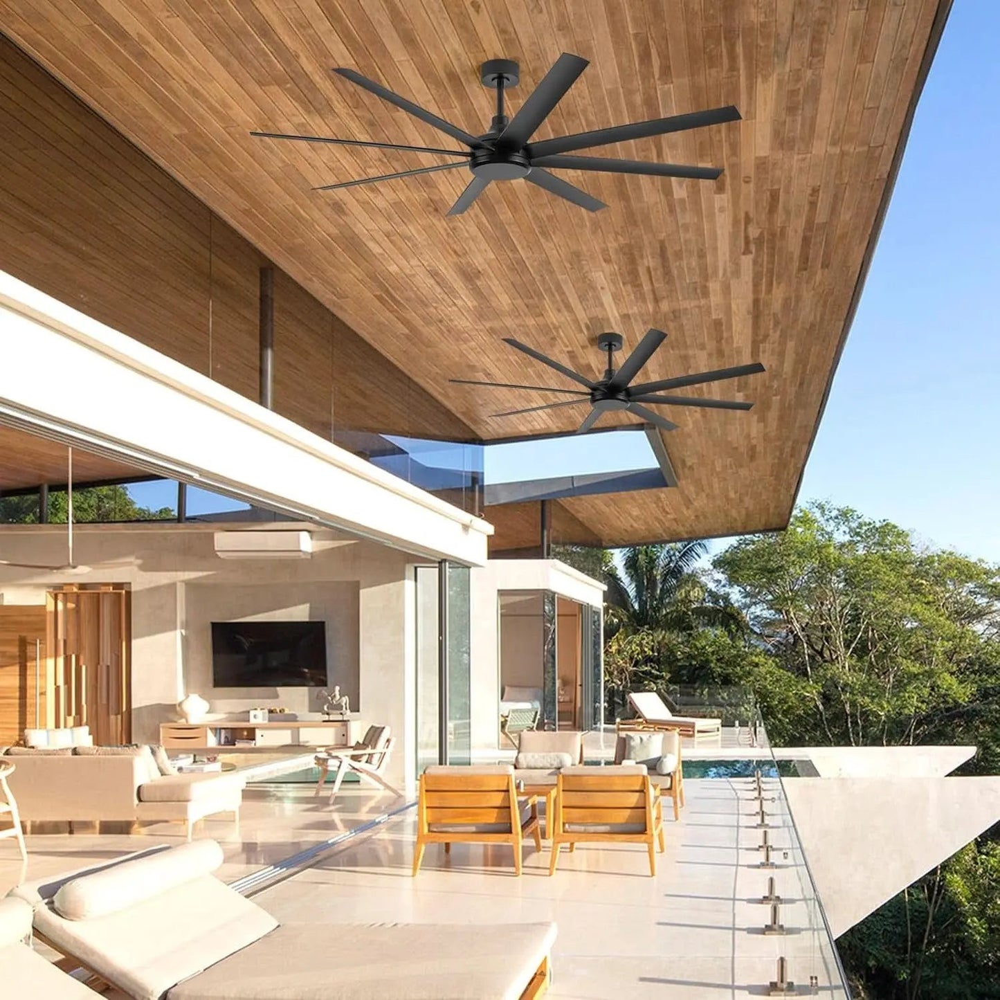 Modern outdoor living space with ceiling fans, furniture, and a view of trees.