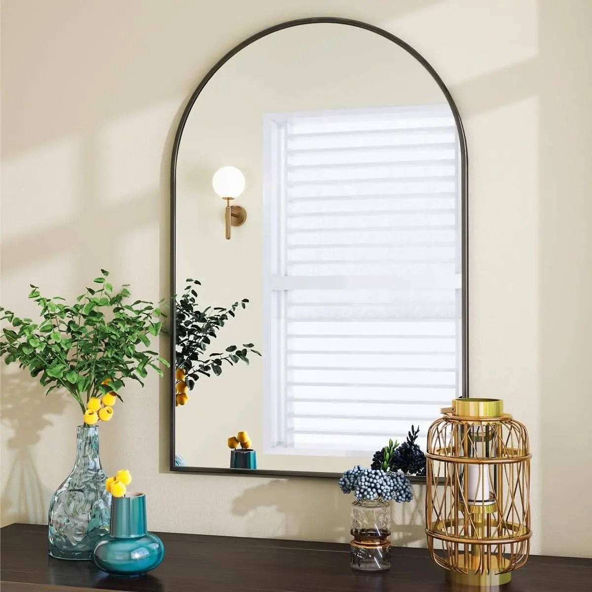 Decorative mirror with a lamp and vases on a table against a neutral wall.