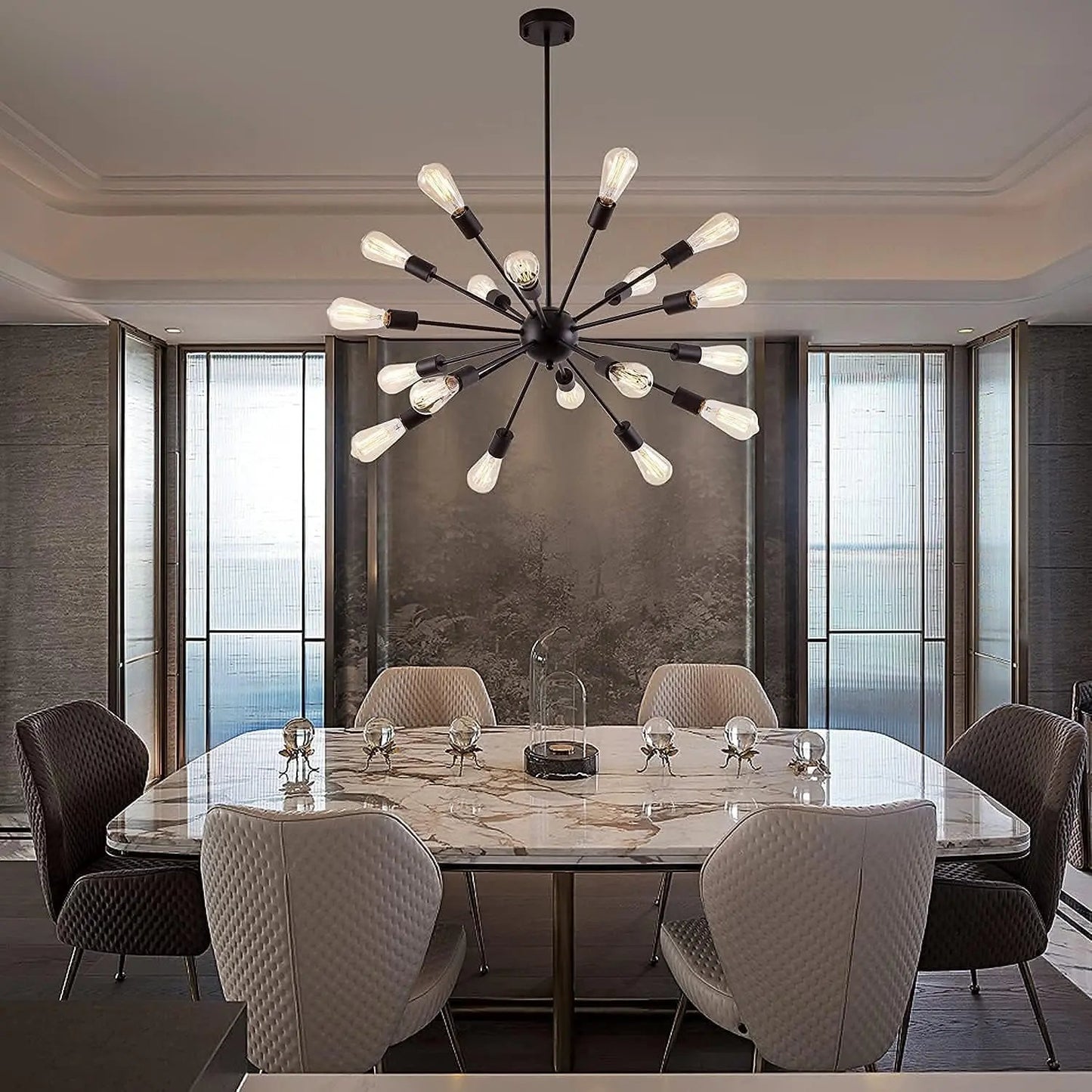 A modern multi-arm sputnik chandelier with clear glass globe bulbs hangs over a marble dining table in a contemporary dining room with gray textured walls and tall windows.