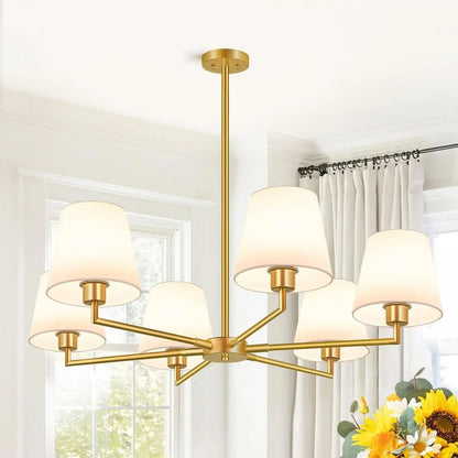 Gold chandelier with white lampshades in a room with curtains and flowers.