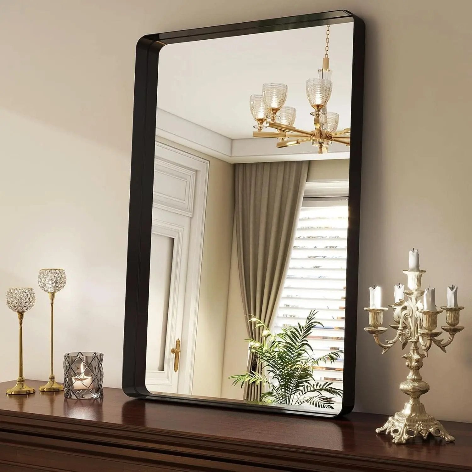 Rectangular mirror with black frame on a wooden surface, reflecting a chandelier and curtains.