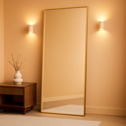 Large floor mirror with gold frame in a room with a side table and vase.