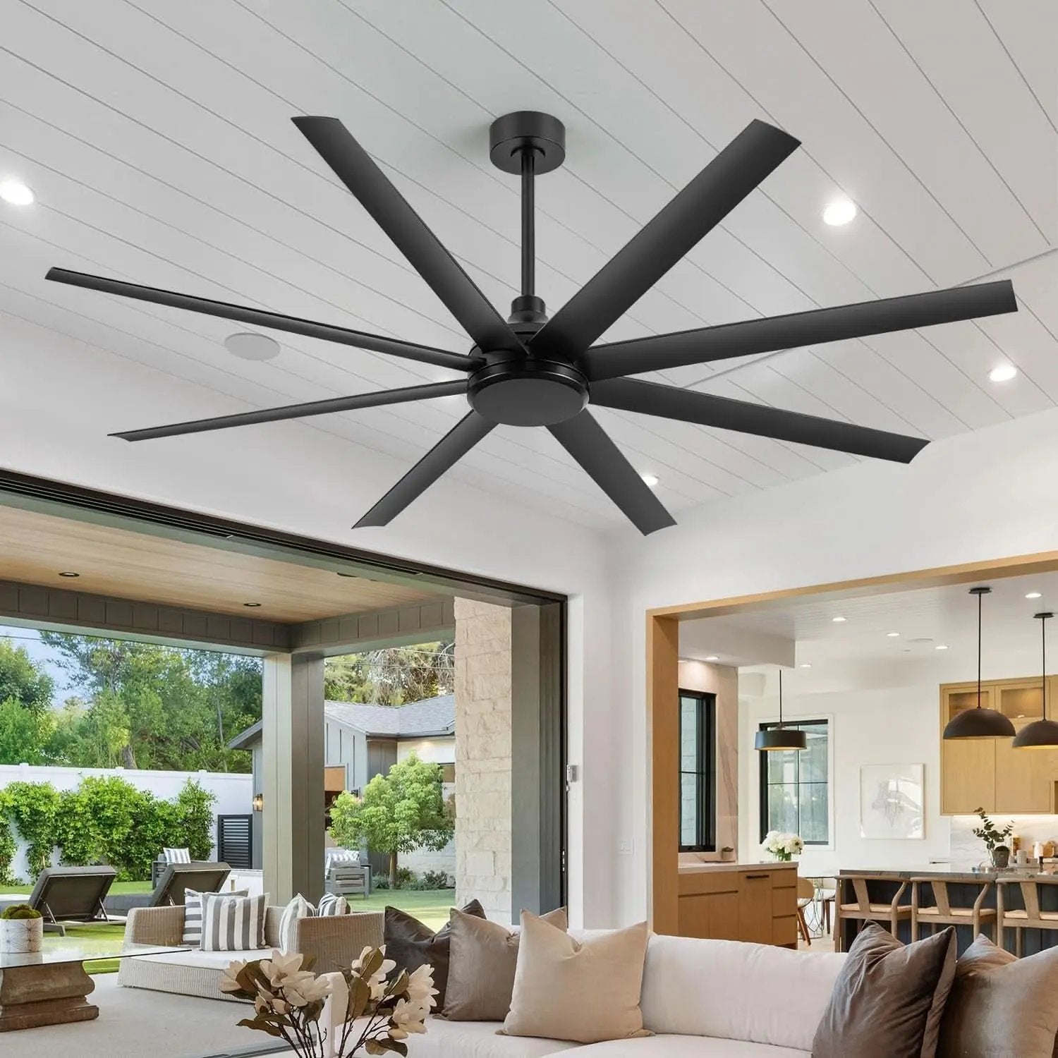 Large black ceiling fan in a modern living room with white walls and large windows.
