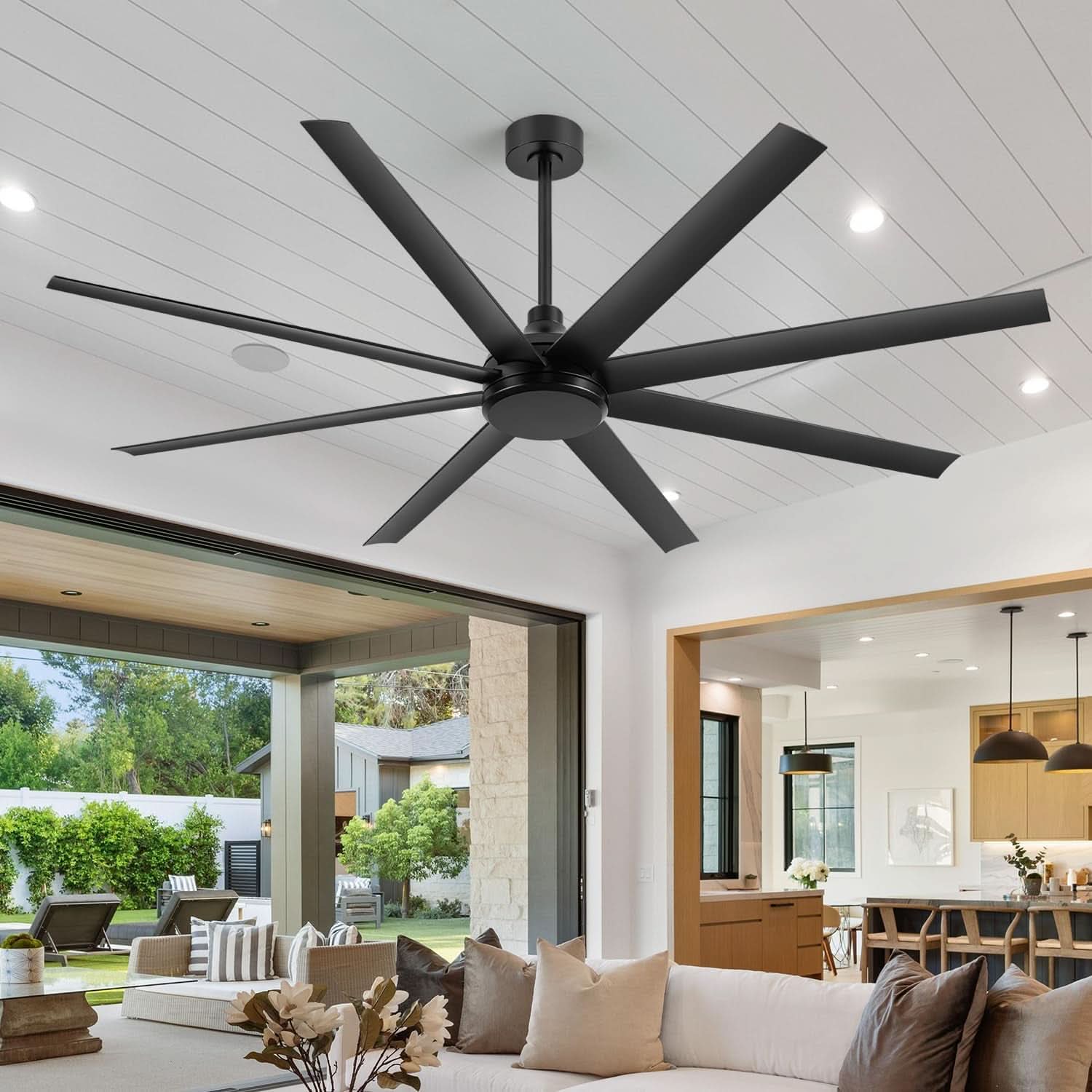 Large black ceiling fan in a modern living room with white walls and large windows.