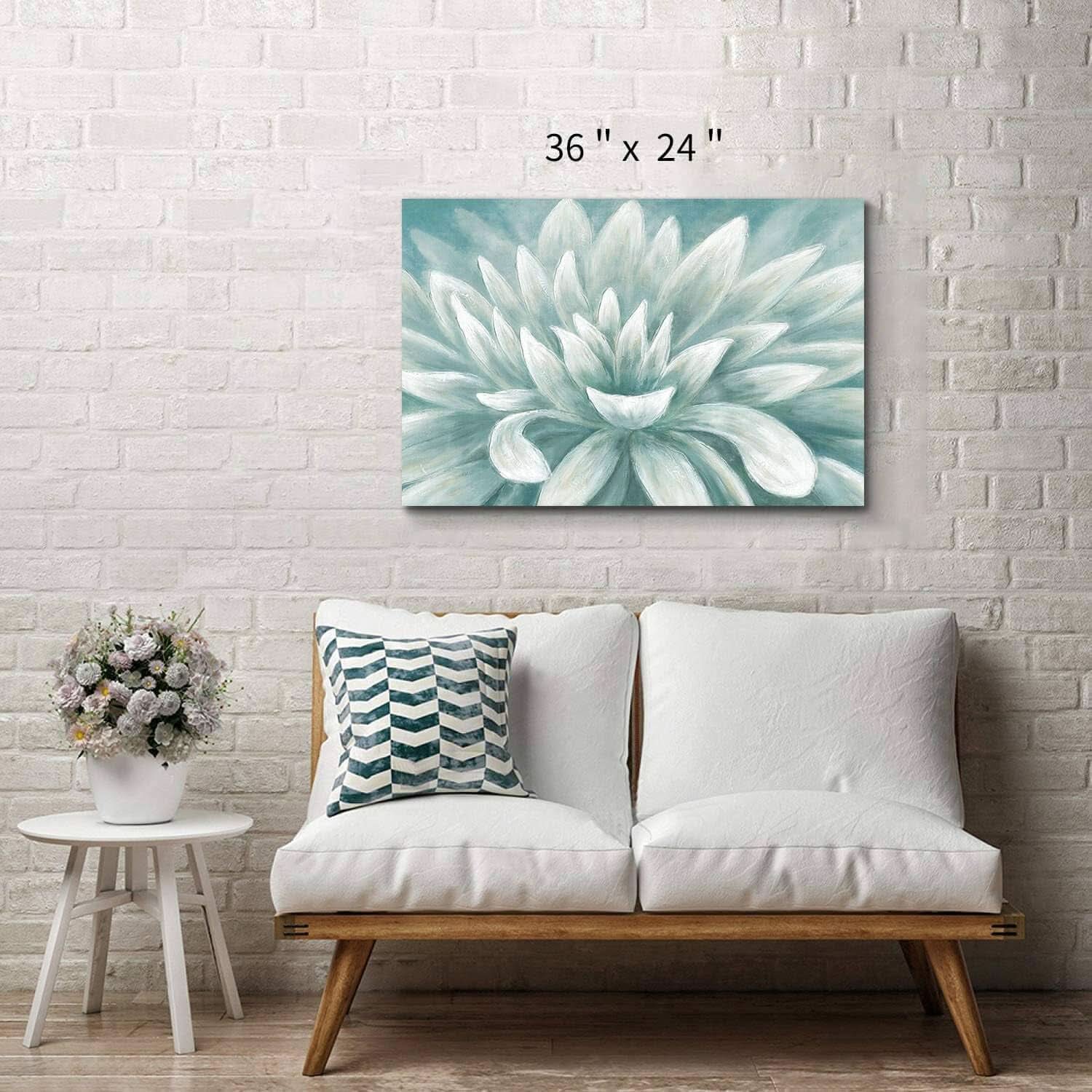 Floral painting above a white sofa with a small table and flowers in a room with a white brick wall.