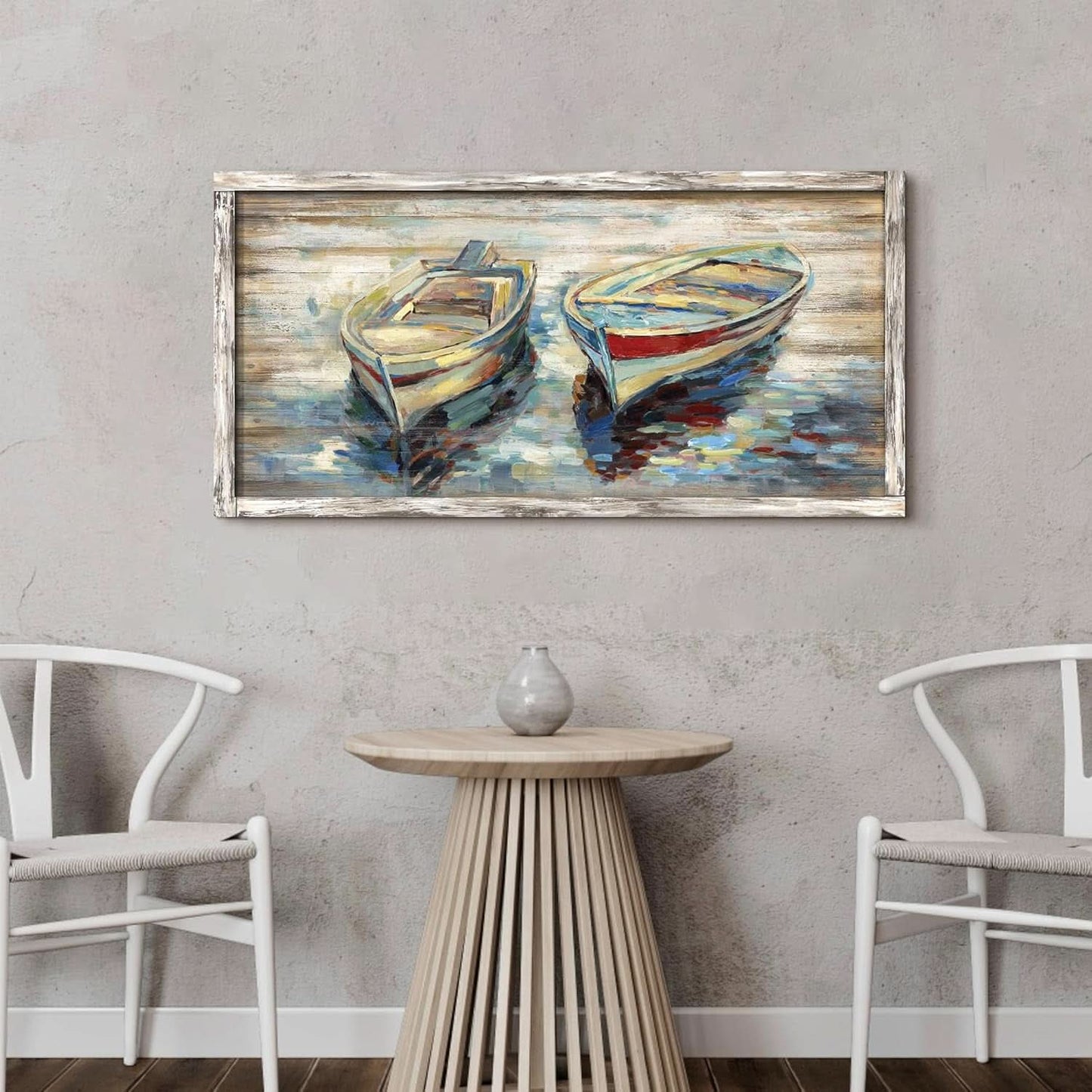 Framed painting of two boats on a wall above a table with chairs.