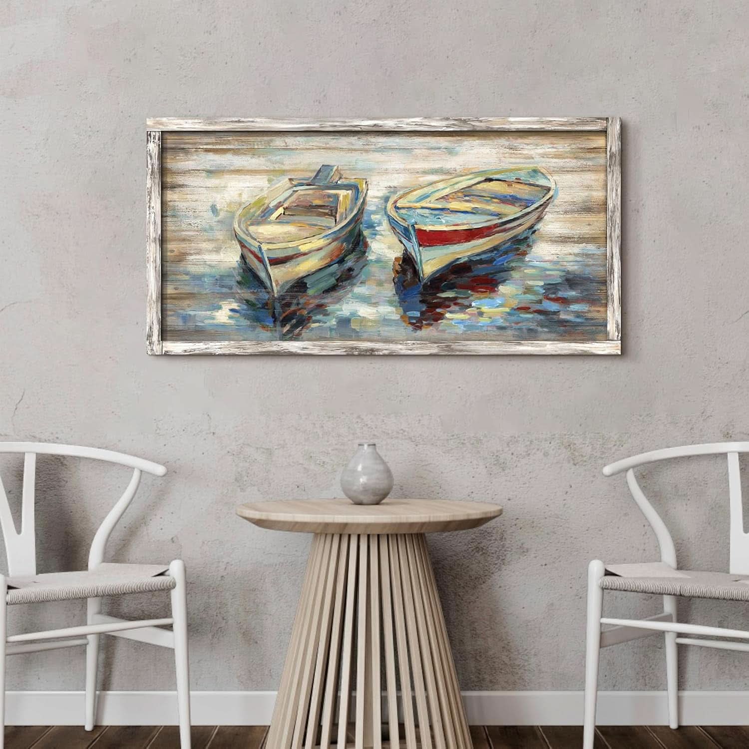 Framed painting of two boats on a wall above a table with chairs.