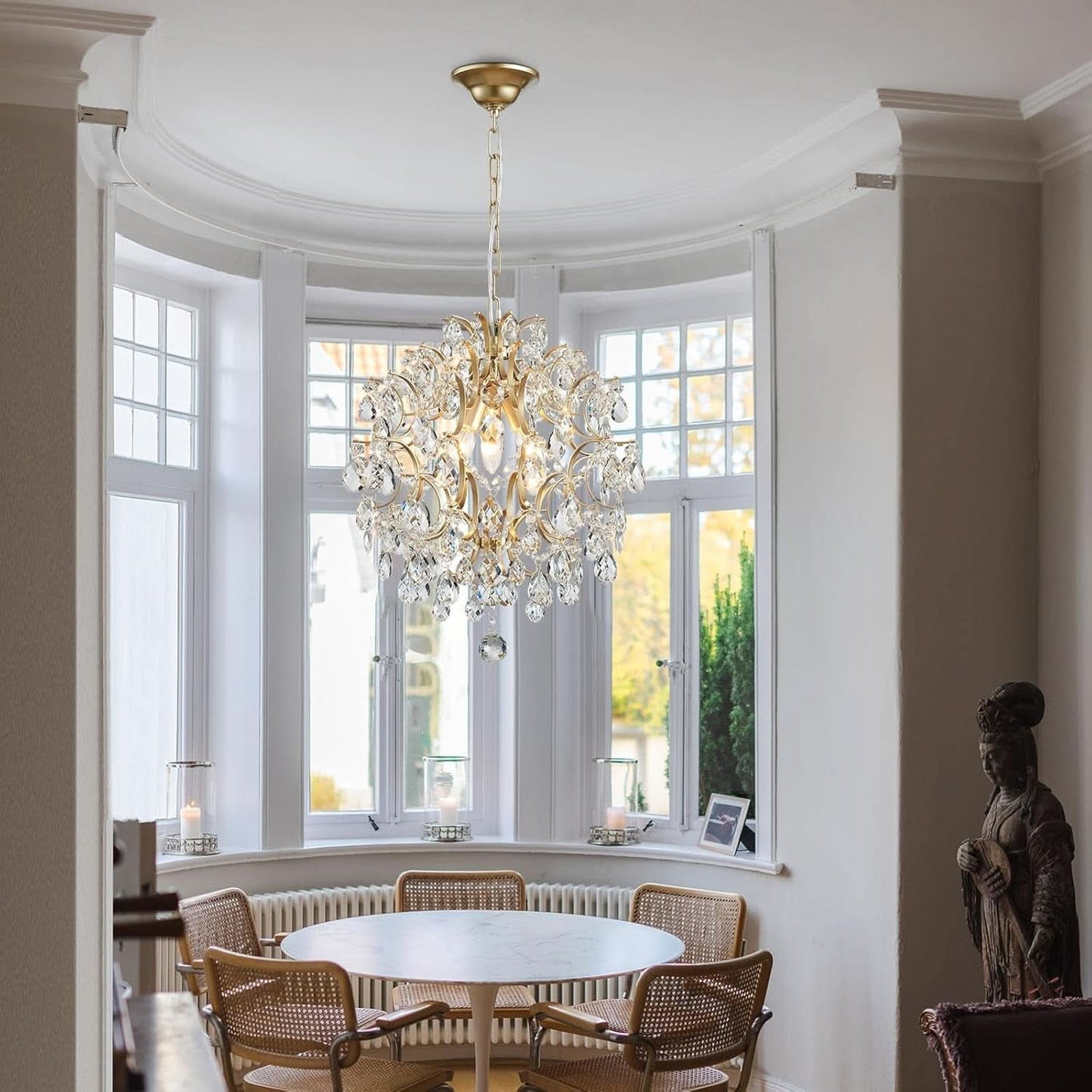 Chandelier hanging in a room with large windows and a statue on a table.